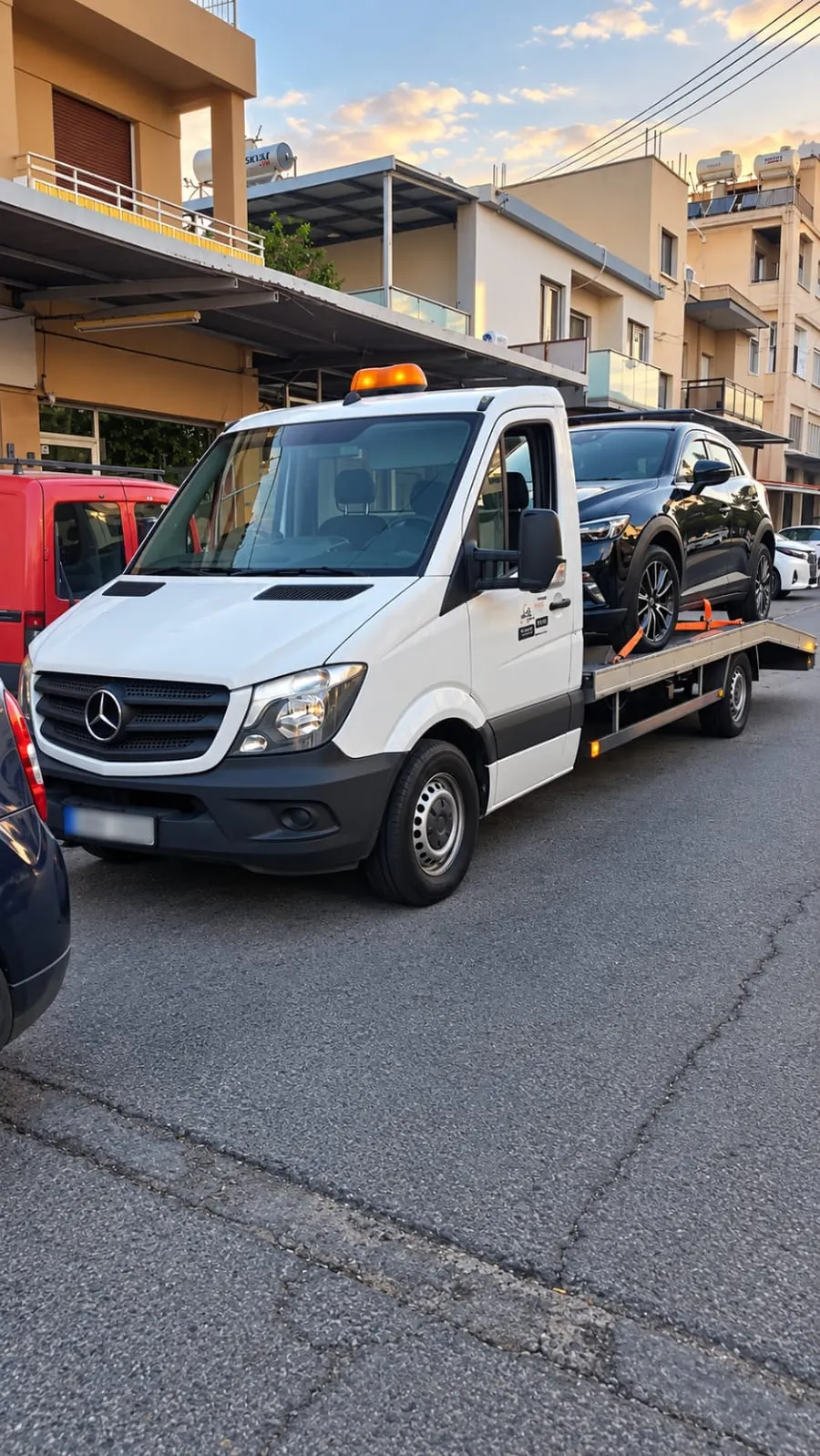 White flatbed recovery truck with a black SUV loaded on the back, parked on a Limassol street